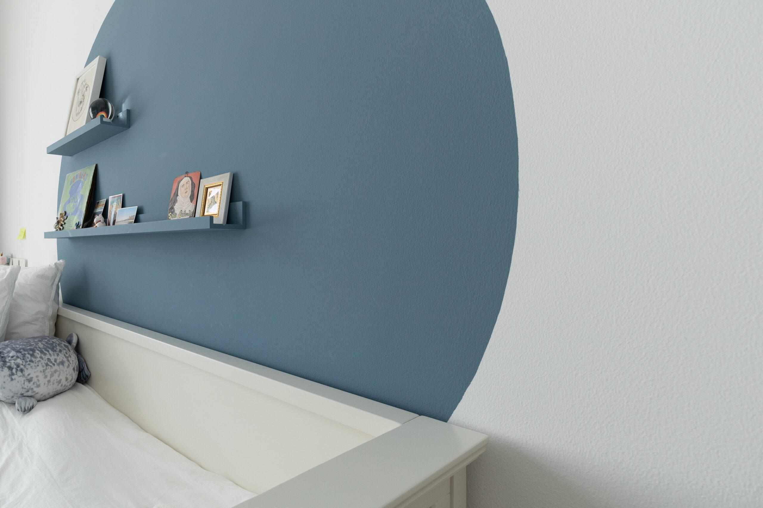 Deep blue painted architectural arch accent wall with two floating display shelves above white bed