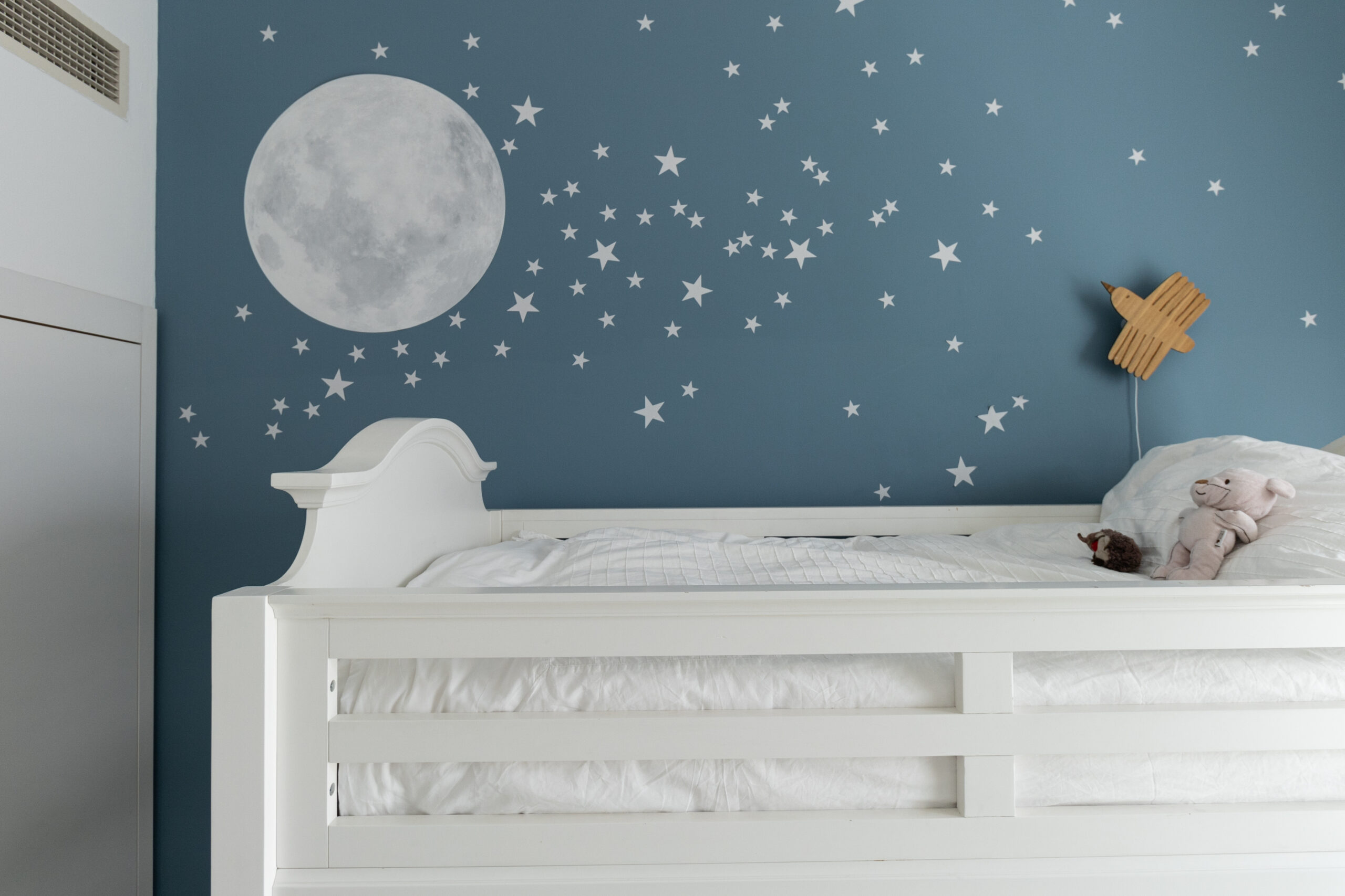 Bespoke blue accent wall with painted celestial moon and stars motif beside a white bed in Palm Jumeirah Apartment